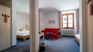 Une chambre d’hôtel avec un lit, un canapé rouge, une petite table, un radiateur et une fenêtre avec des rideaux.