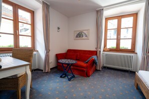 A room with a red sofa, a small round table, a wicker chair, and a radiator.