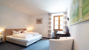 Ein Hotelzimmer mit Bett, Sessel, Tisch und einem Vorhangfenster.
