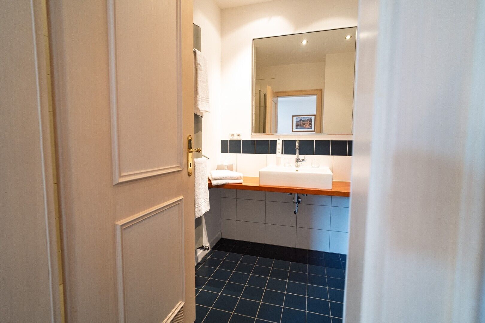 A bathroom with a white sink, a mirror, and a black tiled floor.
