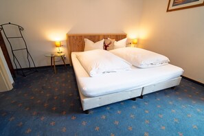 Ein ordentlich bezogenes Bett mit weißen Leinen, zwei Nachttischlampen, ein Holz-Kopfteil und ein gemustertes Teppich.