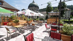 An outdoor patio area with tables and chairs, a large umbrella, and a building with a dome in the background.