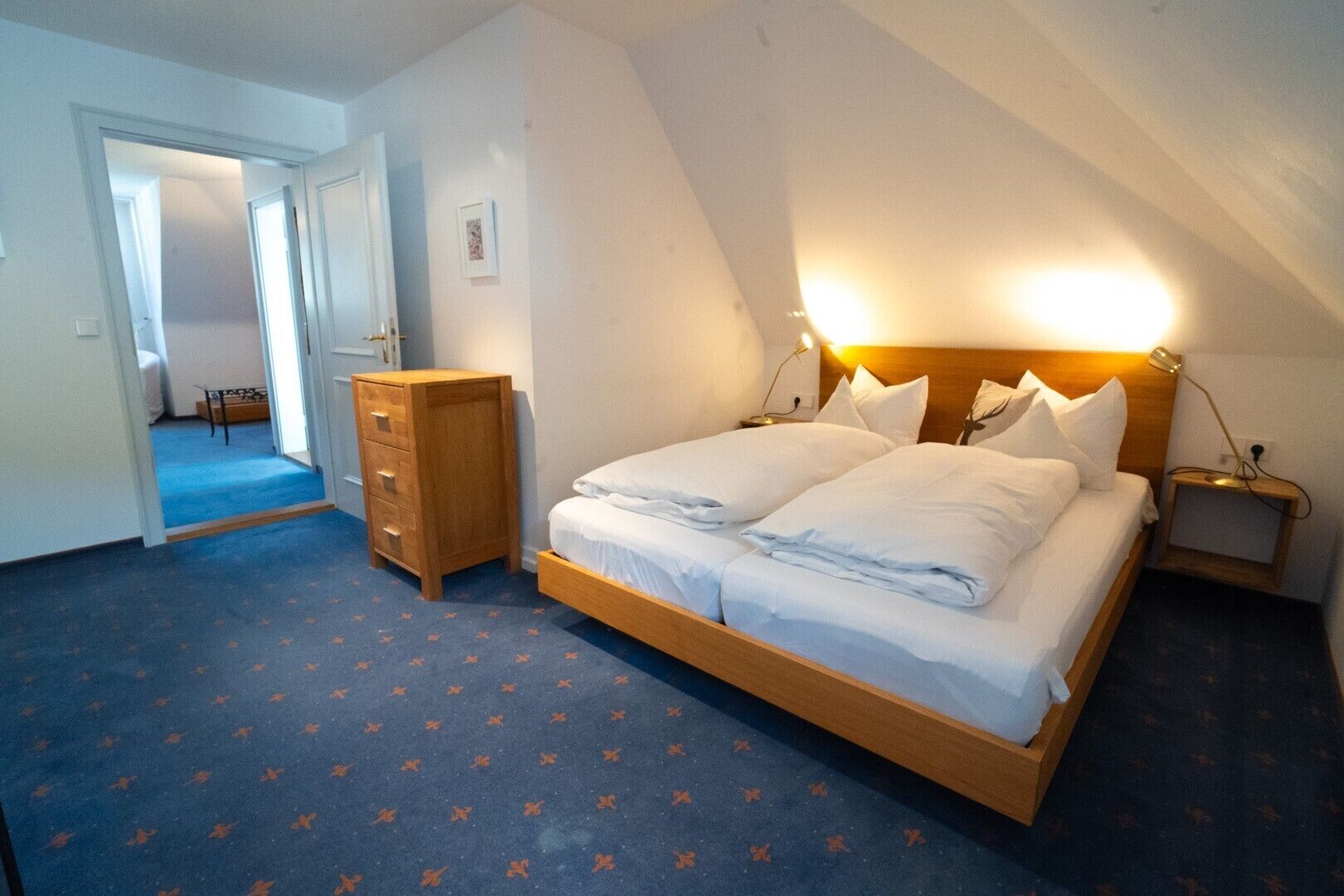 Een slaapkamer met een bed, een kaptafel, nachtkastje en een deur naar een andere kamer.