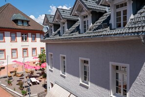 Un bâtiment doté de nombreuses fenêtres et d’un balcon. On y trouve un petit espace extérieur aménagé avec des tables et des chaises.