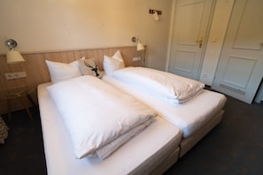 Un lit double avec une literie blanche, une table de chevet, une lampe et une porte.