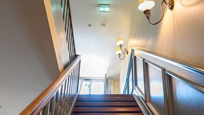 A wooden staircase with a metal railing, wall sconces, and a ceiling light fixture. - Room 'Double Room 8' with Shared Garden and Wi-Fi (St Blasien)