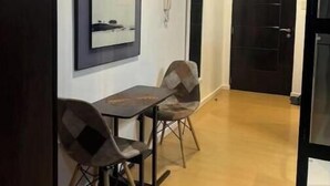 A hallway with a dining table and chairs, a framed artwork on the wall, and a door leading to another room. - Cozy studio unit in Avant BGC (Taguig)