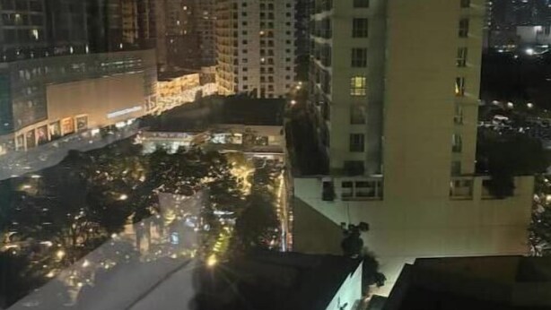 A nighttime view of a high-rise building with multiple floors, illuminated windows, and a well-lit courtyard area. - Cozy studio unit in Avant BGC (Taguig)