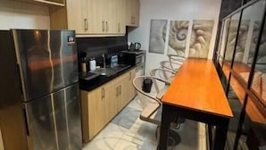 A compact kitchen with modern appliances, a dining area with a wooden table, and a view of the city through the window. - Cozy studio unit in Avant BGC (Taguig)