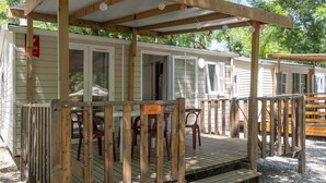 En campingvogn med træterrasse, udendørs møbler og en overdækket terrasse.