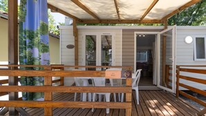 A wooden deck with a covered seating area, a dining table with chairs, and a view into a room with a window.