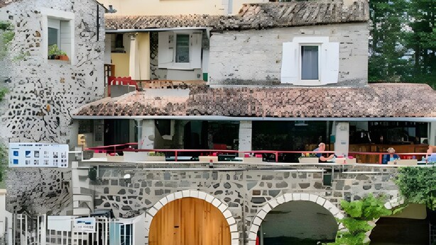 A pool area with lounge chairs, a stone bridge, and a building with a restaurant.