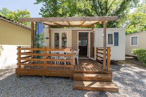A wooden deck with a table and chairs, a covered seating area, and a small building with a door.