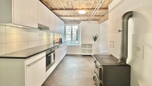 A modern kitchen with white cabinetry, a stainless steel countertop, a built-in oven, and a large window providing natural light. - Business Apartment Oberbipp (Oberbipp)