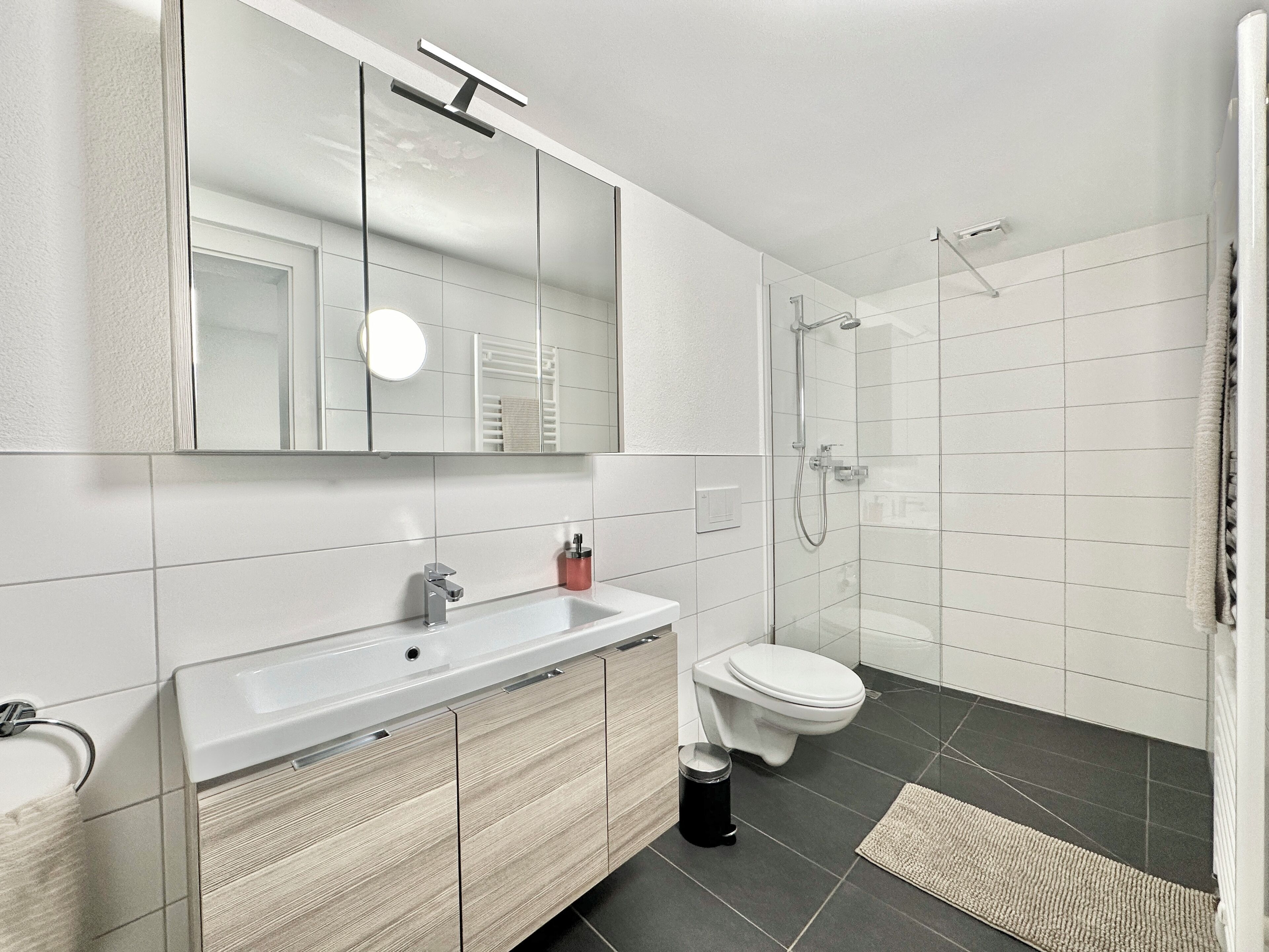 Ein modernes Badezimmer mit Waschbecken, Spiegel und Toilette in Weiß.