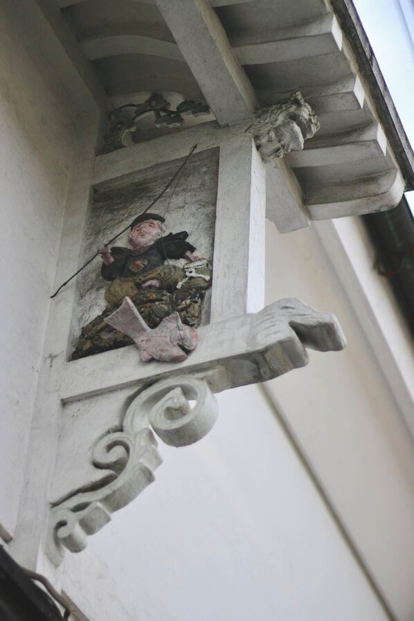 A corner of a building with a decorative stone balustrade and a small window with a decorative stone frame.