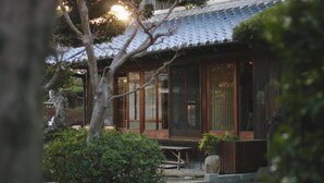 A traditional Japanese-style building with a tiled roof, large wooden sliding doors, and a small garden area with a bench and potted plants. - 120-years-old house in Kobe with authentic Japanese decor & cultural experiences (Kobe)