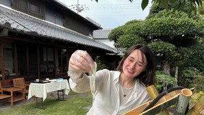 A person holding a traditional bamboo flute outdoors, with a wooden building and a table with chairs in the background. - 120-years-old house in Kobe with authentic Japanese decor & cultural experiences (Kobe)