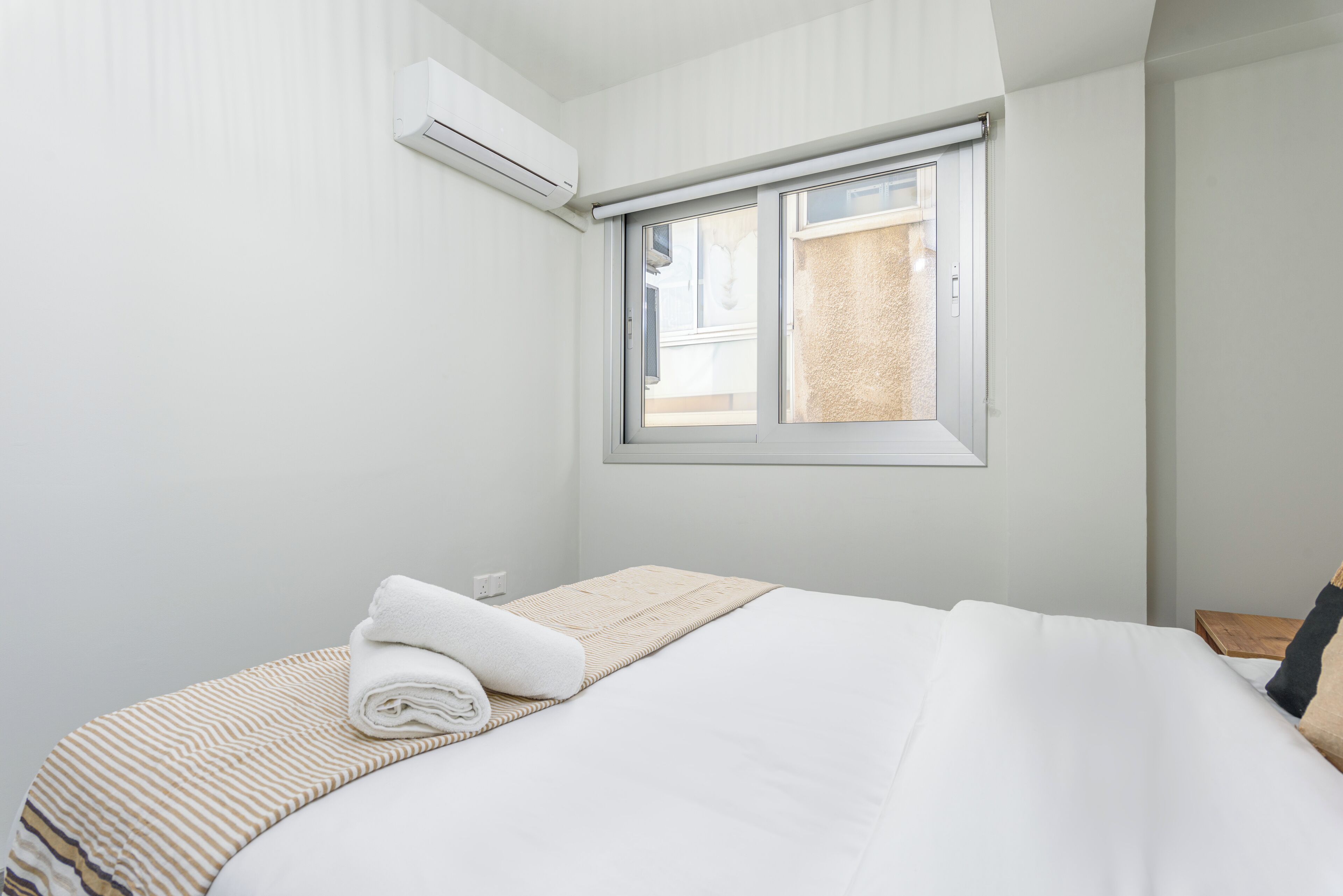 A neatly made bed with a rolled white towel, a striped blanket, and a beige throw.