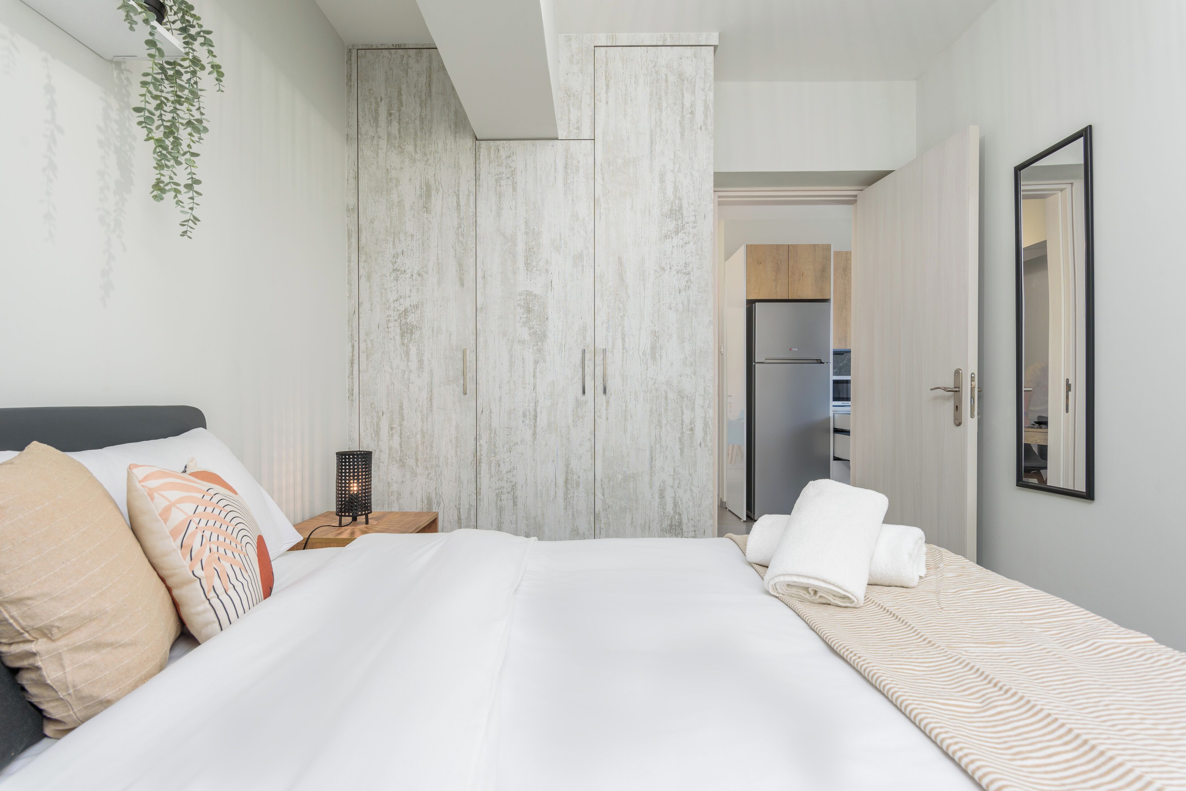 Une chambre d’hôtel moderne avec un grand lit, une table de chevet, une plante suspendue et une vue sur la cuisine.