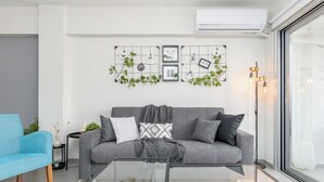 A modern living room with a grey sofa, a glass coffee table, and a wall-mounted picture frame with greenery. - Amore 2-BR Apt By Finikoudes (Larnaca)