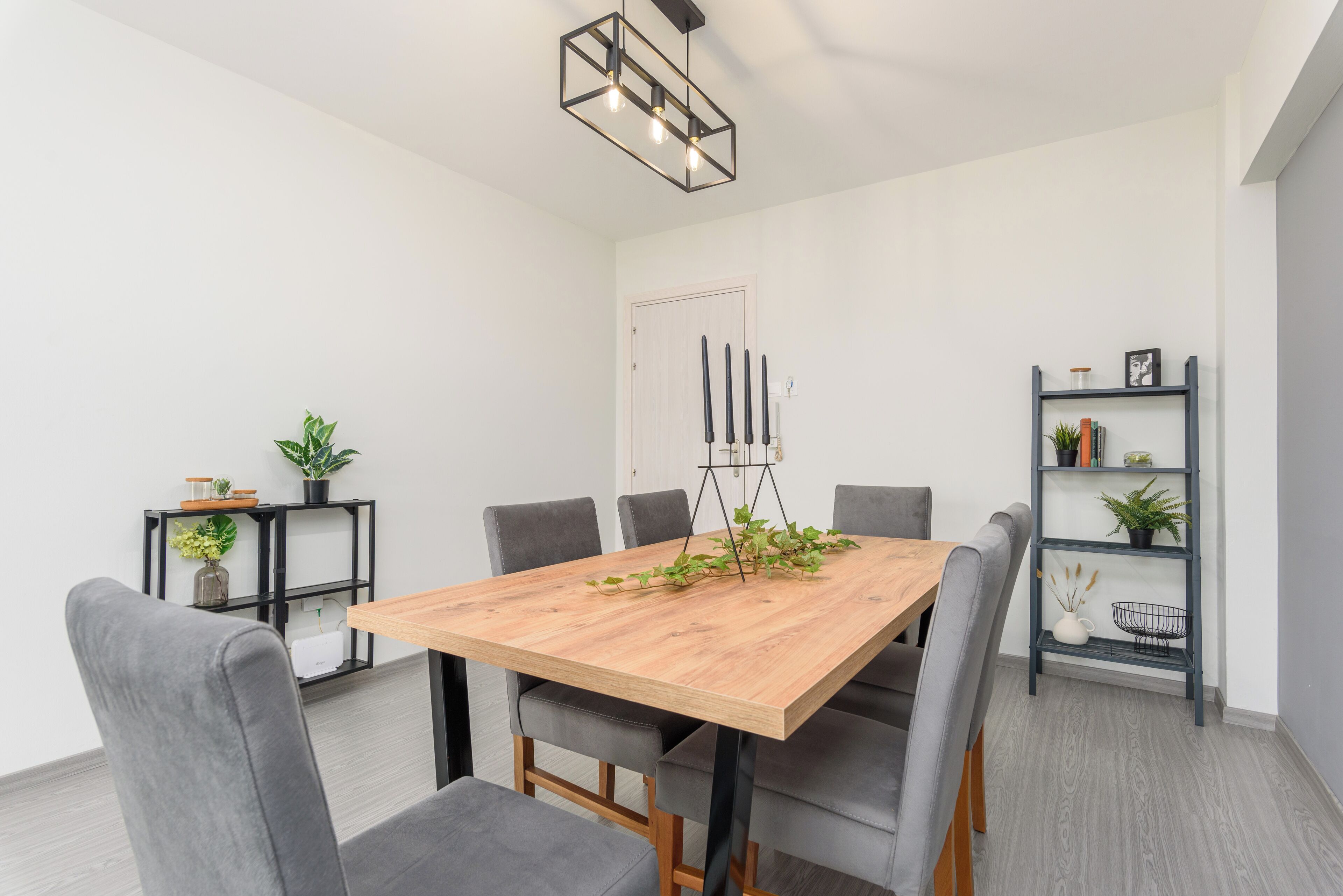Un espace repas moderne avec une table en bois, six chaises grises à revêtement, une bibliothèque en métal noir et un luminaire suspendu.
