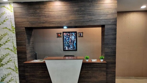 A reception desk with a dark wood finish, a white counter, and two small potted plants. - Hotel Shri Bhaskar (Bareilly)