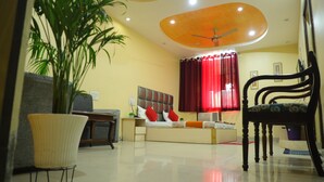 A modern living room with a sofa, a chair, a bed, a ceiling fan, and a potted plant. - Hotel Shri Bhaskar (Bareilly)