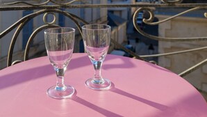 Une table rose avec deux verres vides, sur un balcon donnant sur une vue panoramique de la ville, avec ses bâtiments historiques.