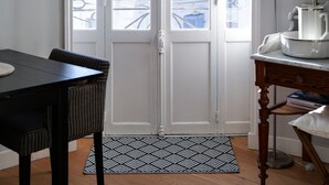 Une pièce avec une porte blanche, une table à manger avec des chaises, un lampadaire et un tapis à motifs.