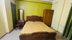 A bedroom with a bed, a dresser, a mirror, and a wardrobe. - Prashi Homes (Varanasi)