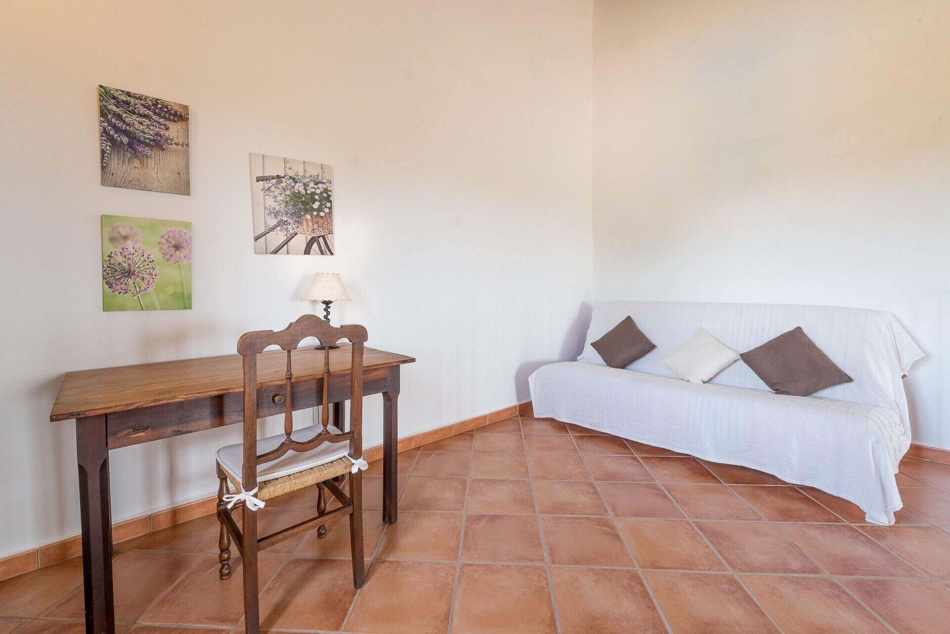 Une pièce comprenant un bureau en bois, une chaise, un canapé blanc et trois tableaux accrochés au mur.