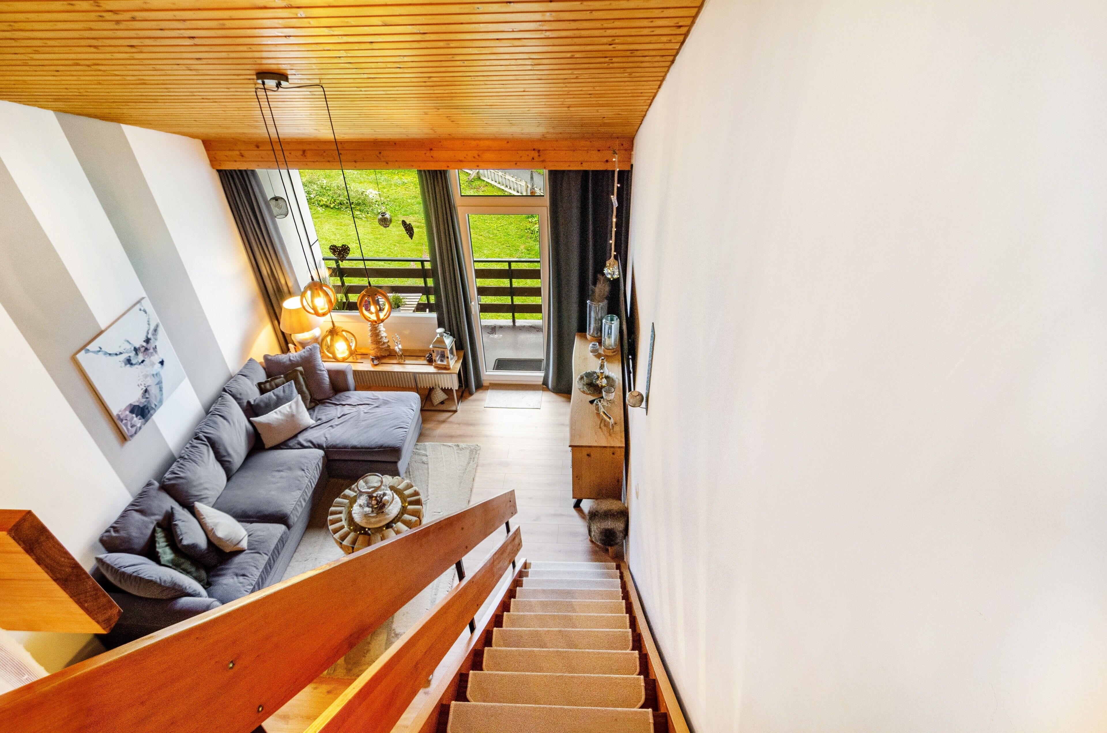 A staircase leading to a living area with a sofa, wooden railing, and a view of the outdoors.