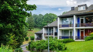 Une maison à deux étages avec un balcon, entourée de verdure et d’une clôture en bois.