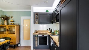 Une cuisine compacte dotée d’un four encastré, d’une table à manger en bois et d’un petit meuble contenant des objets décoratifs.