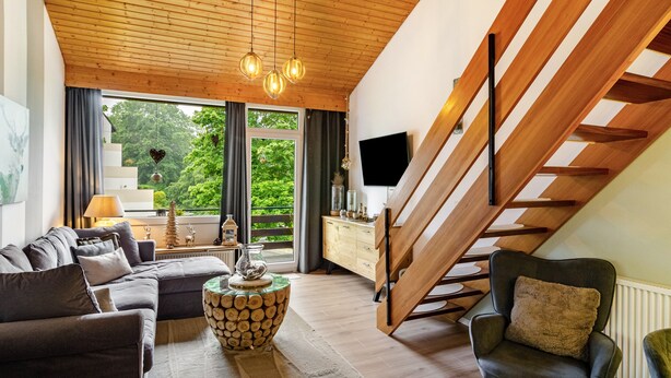 Un salon moderne avec un plafond en bois, un escalier, un canapé, une table basse et un téléviseur.