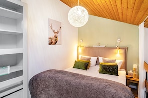 A bedroom with a bed, bedside tables, a wall-mounted light fixture, and a picture of a deer.
