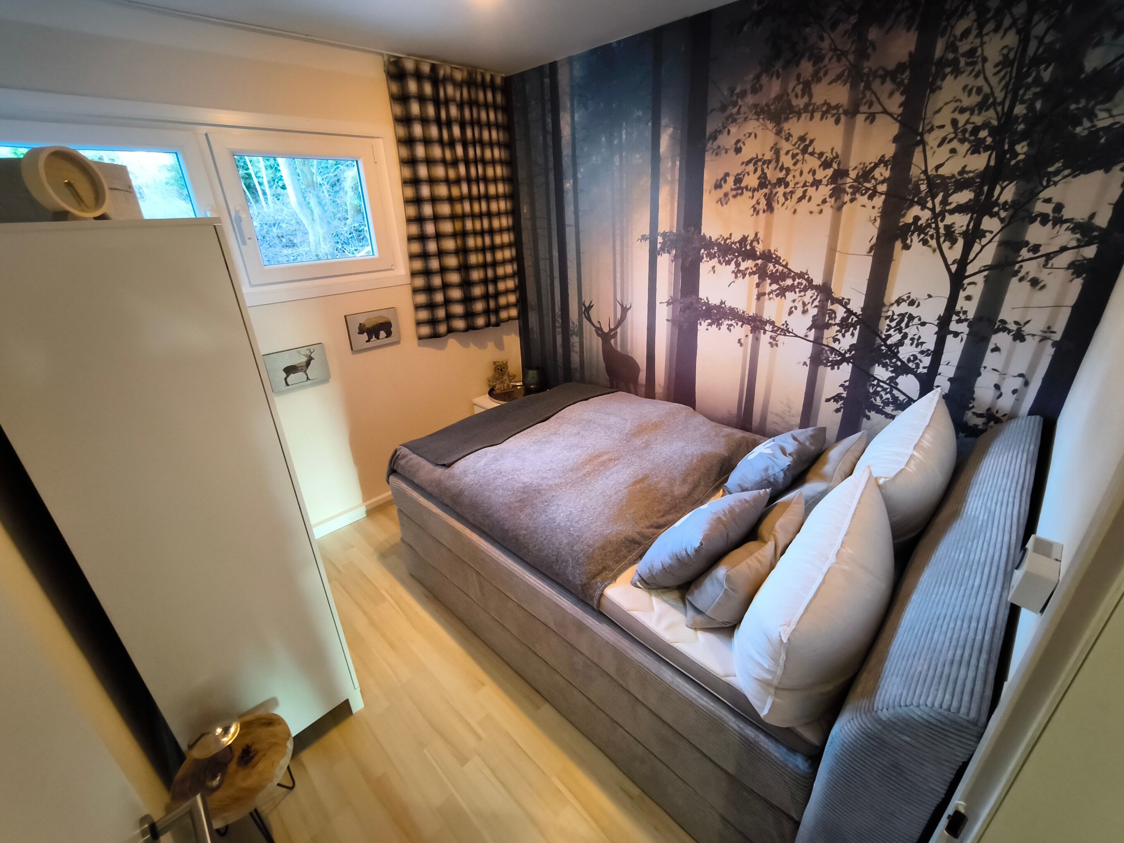 A bedroom with a bed, a window, a door, and a wall with a forest mural.