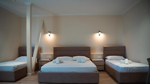 A hotel room with three single beds, each with a nightstand and a lamp. The room has a wooden floor and beige walls. - Okej Hotel (Golem)