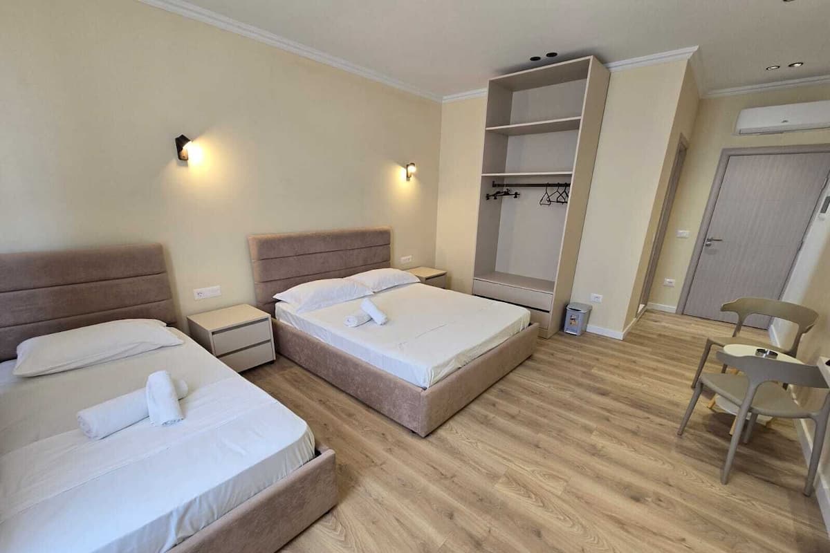 A hotel room with two beds, a wardrobe, a chair, and a small table.
