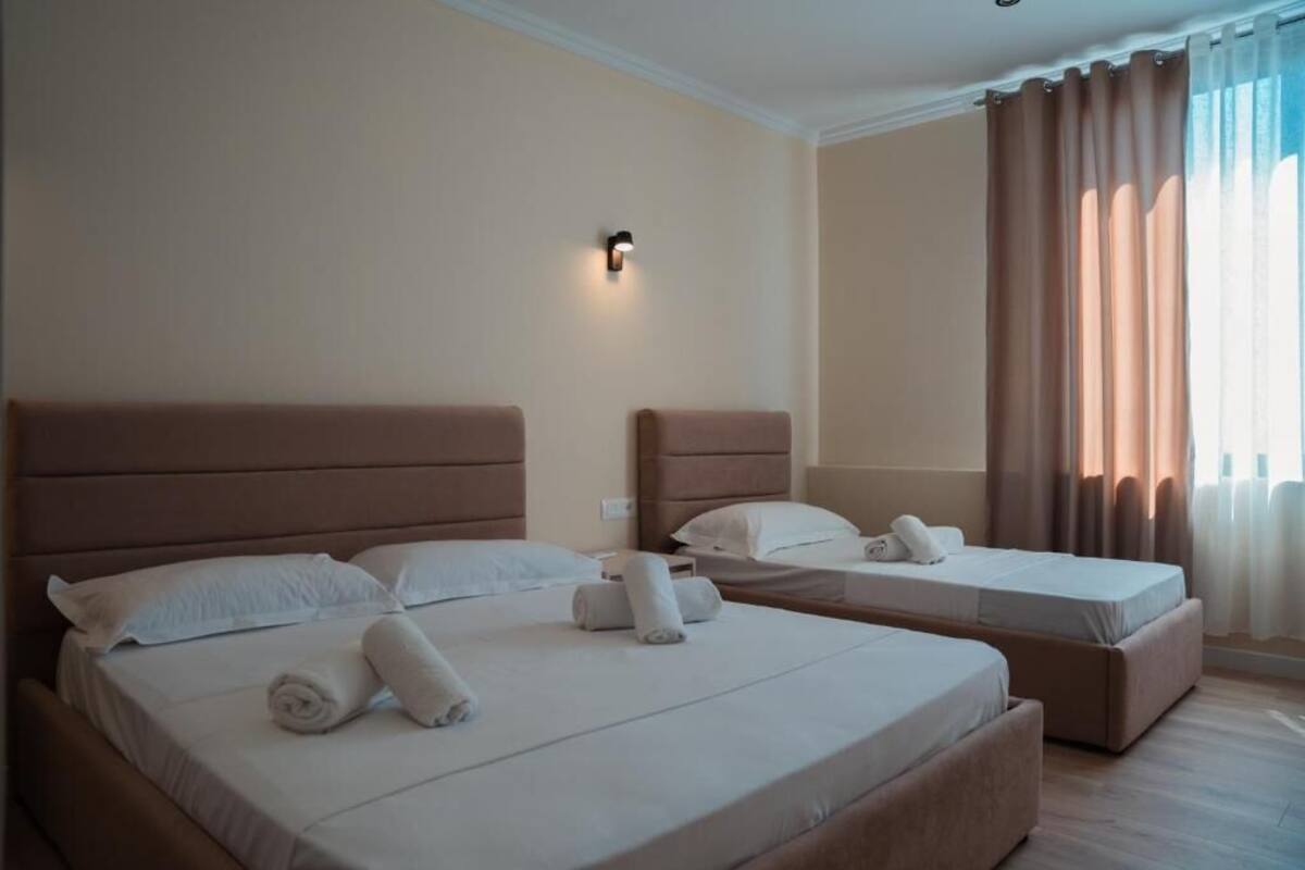 A hotel room with two beds, each with a headboard, a wall-mounted light, and a window with curtains.