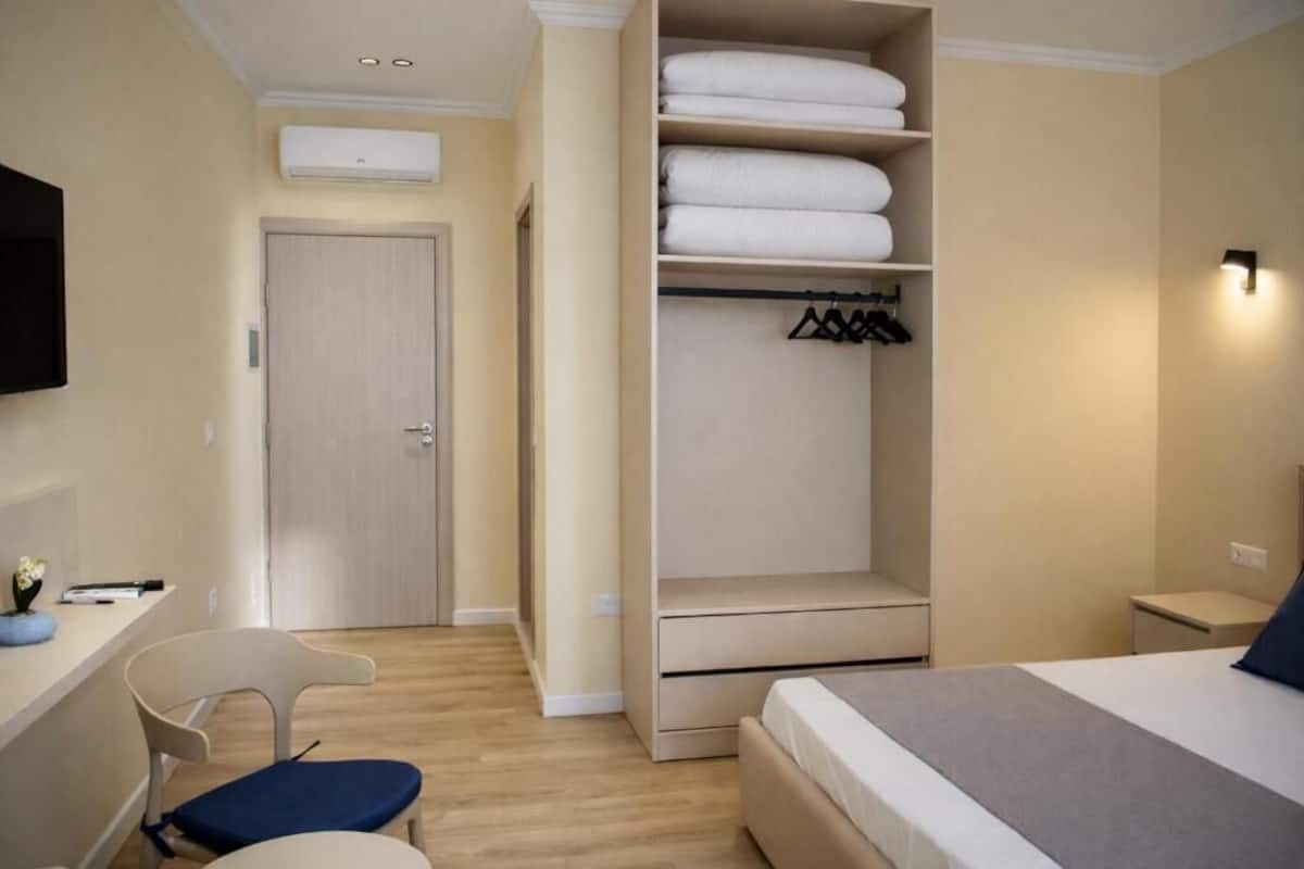 A bedroom with a bed, a desk with a chair, a wardrobe, and a wall-mounted TV.