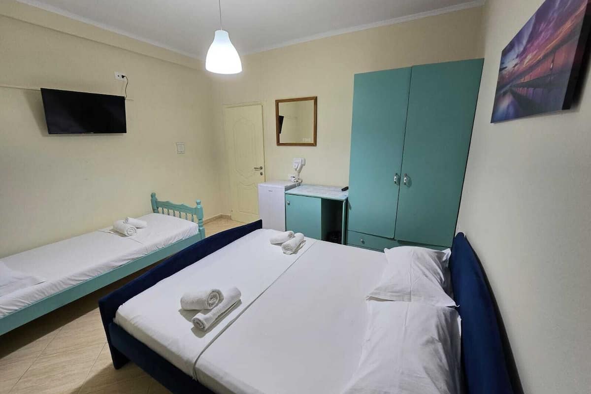 A room with two single beds, a desk with a chair, a television, a wardrobe, and a painting on the wall.