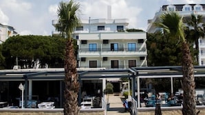 A modern building with a flat roof, multiple windows, and a covered outdoor seating area with tables and chairs. - Okej Hotel (Golem)