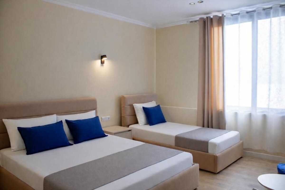 A hotel room with two beds, a small table, and a window with curtains.