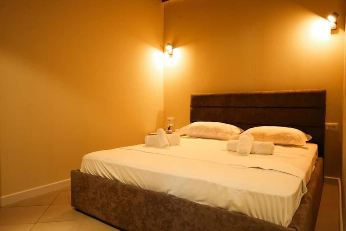 A neatly made bed with white linens and pillows, two wall-mounted light fixtures, and a dark headboard.