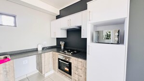 A modern kitchen with white cabinets, a black countertop, a gas stove, and a microwave.