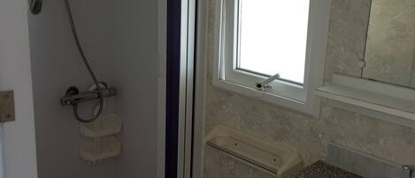 A bathroom with a shower, a sink, and a window.