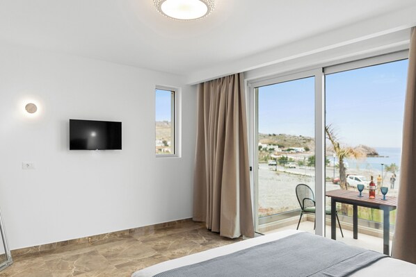Une chambre d’hôtel avec un lit, une télévision, une table avec des verres et une vue sur la plage.