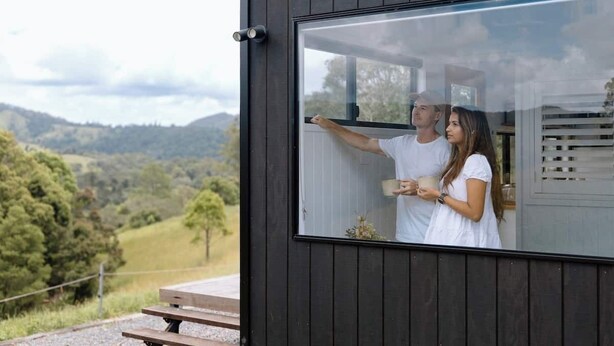 A modern building with a large window, a wooden deck, and a scenic view of hills and trees. - The Cabin@KC. Peaceful Tiny Home Escape on 60 Acres near Mapleton (Queensland)